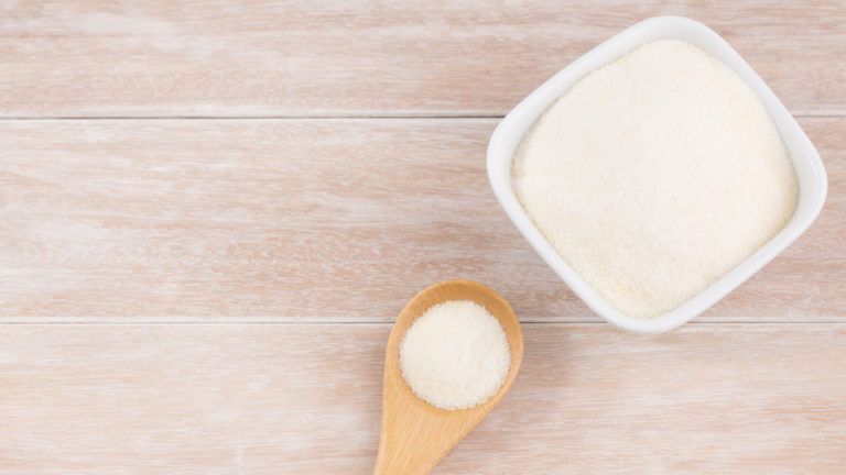 A wooden spoon and ceramic bowl filled with collagen powder.